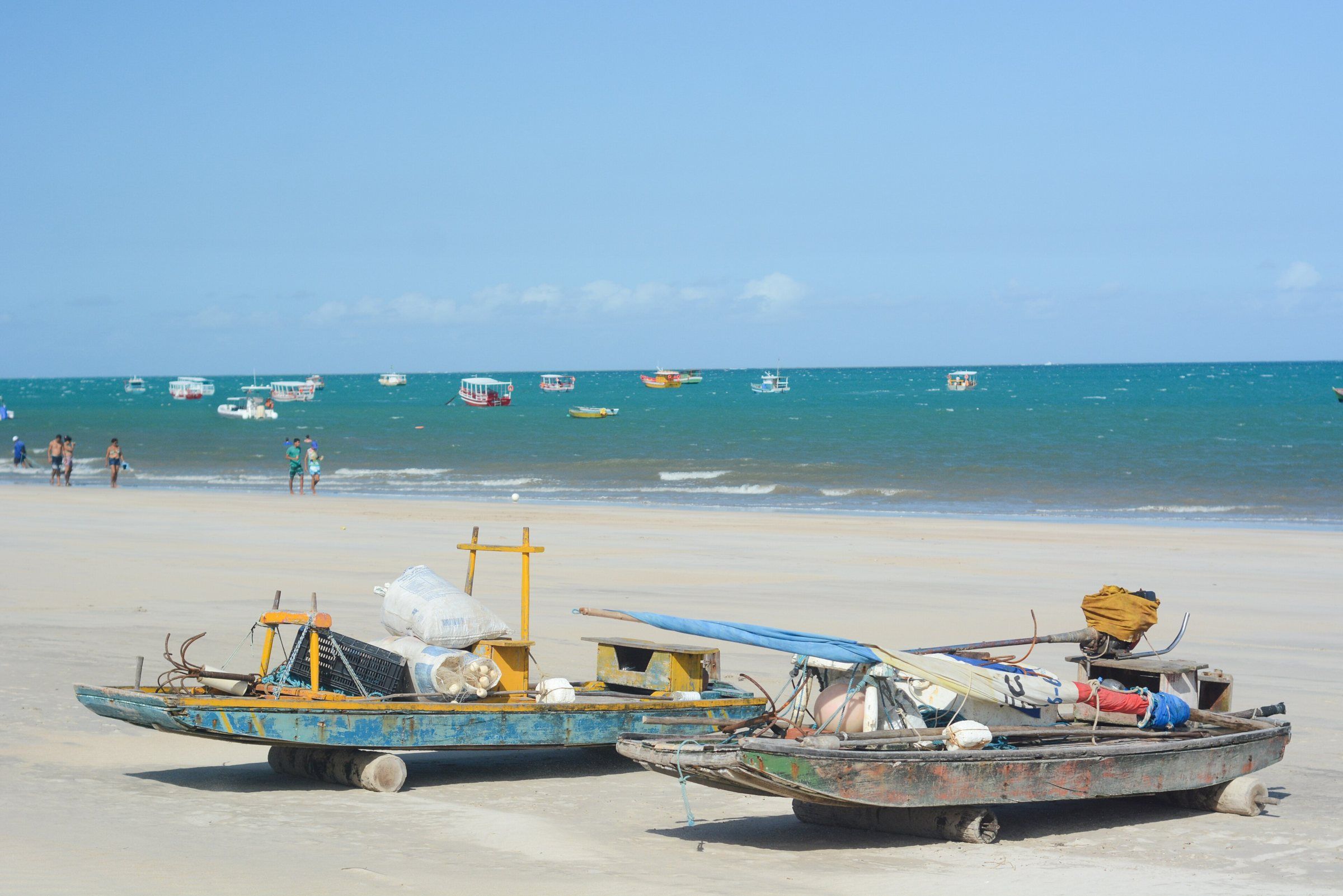 Jangadas e barcos de pesca na areia da Praia de Maragogi, com lanchas no mar turquesa