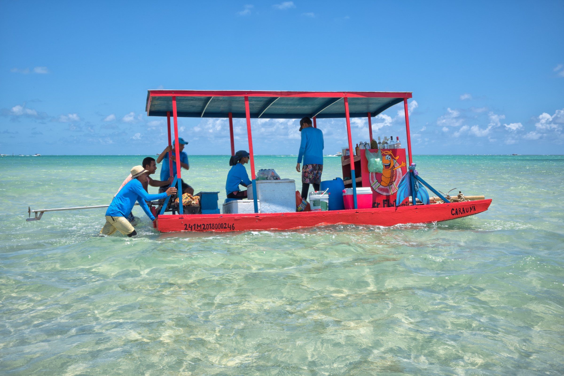 Barco de apoio e banhistas na água rasa e cristalina do Caminho de Moisés, em Maragogi